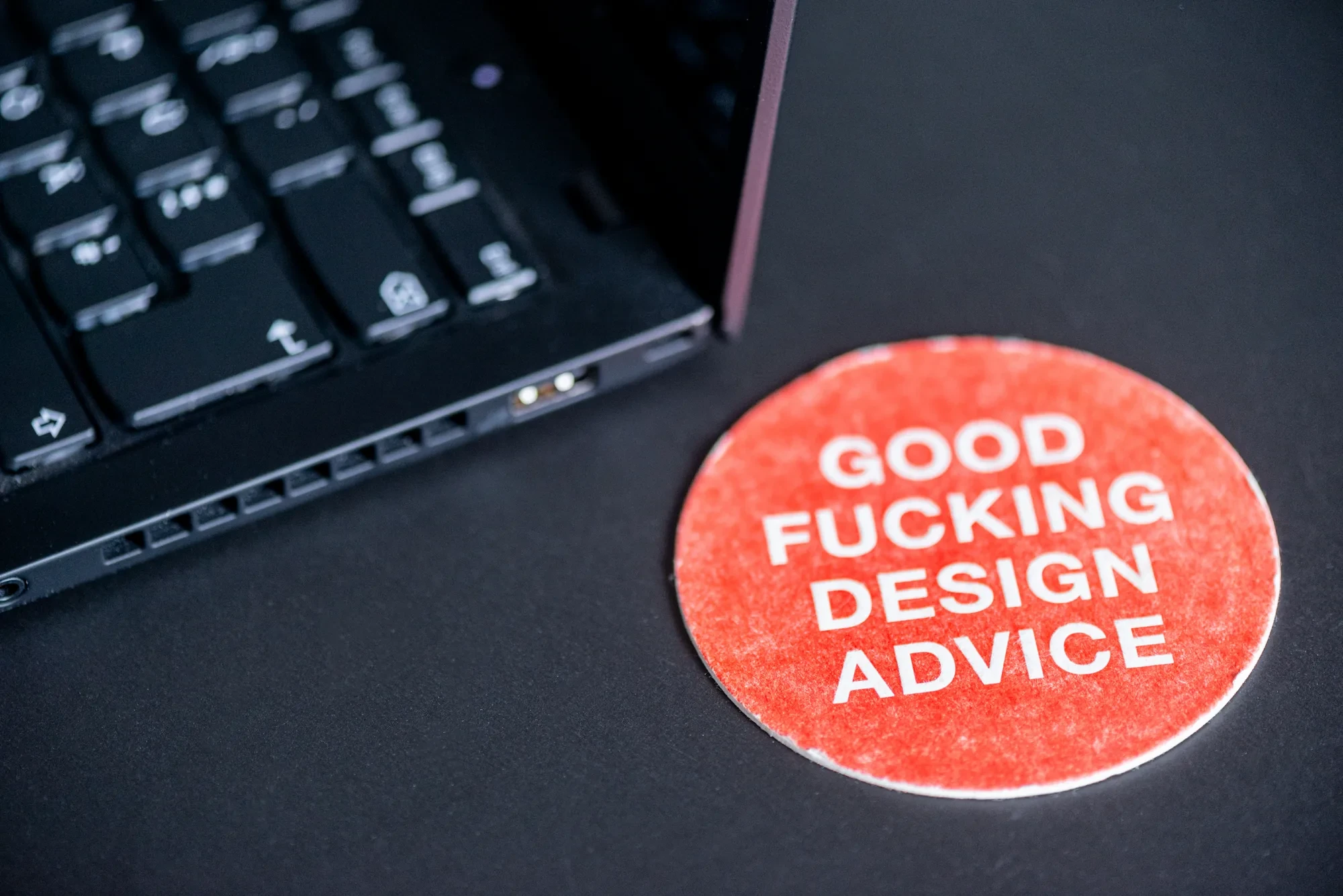 Ein runder Sticker mit einem Design-Spruch neben einer Laptop-Tastatur
