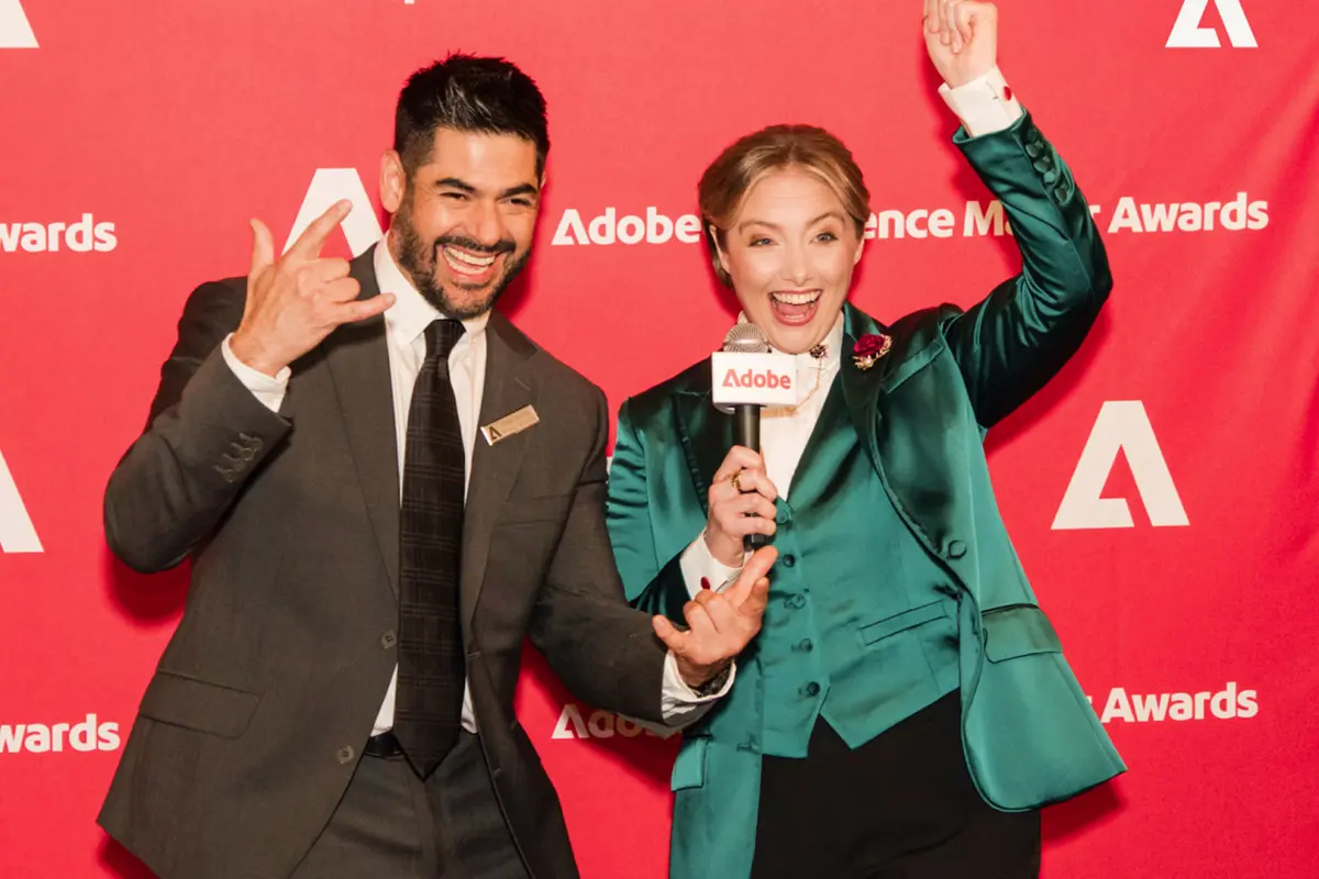 Two hosts celebrating in front of the Adobe Experience Maker Awards wall