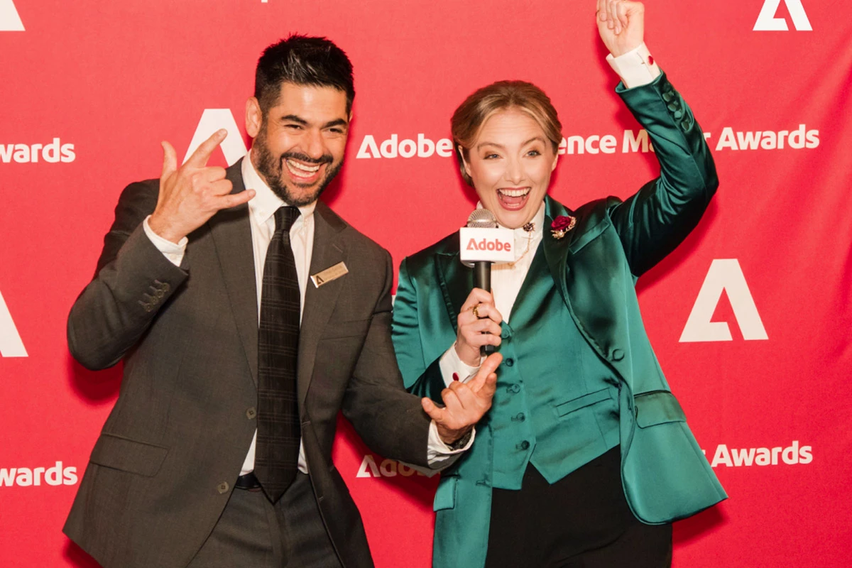 Two hosts celebrating in front of the Adobe Experience Maker Awards wall