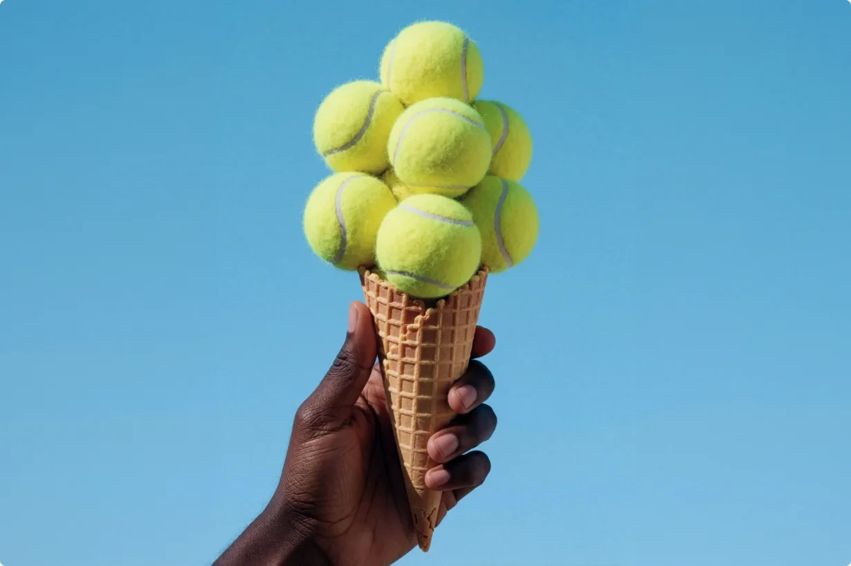A hand holding a cone stacked with tennis balls against a blue sky