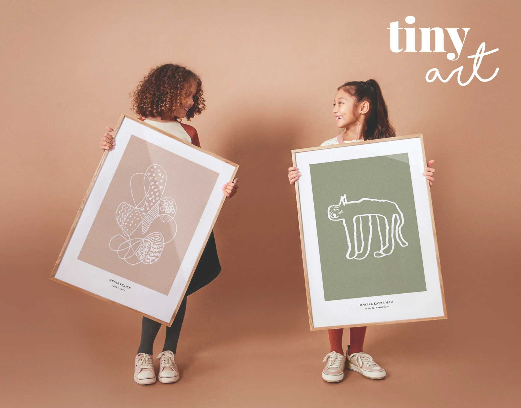 Two children holding up framed art prints made from their own drawings